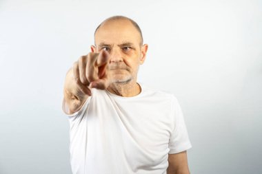 Beyaz tişörtlü kendinden emin bir adam tarafsız bir arkaplan üzerinden izleyiciyi işaret ediyor. Görüntü kararlılık, odaklanma ve bağlantı iletir. Otorite ve iletişim içeren kavramlar için ideal.