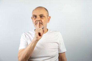 Beyaz gömlekli olgun bir adam sessiz bir jest yapıyor. Parmağını dudaklarına dayayıp düşünceli ve ciddi görünürken mahremiyeti, düşünmeyi ya da sessizliği öneriyor..