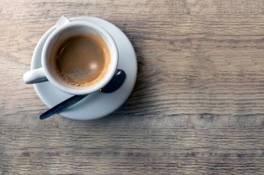 Kırsal bir ahşap masada taze demlenmiş kahveyle dolu beyaz bir seramik bardak. Rahatlatıcı bir sabah ya da iş arası için mükemmel bir ortam. Basitliği, sıcaklığı ve espresso kokusunu özetlemek için..