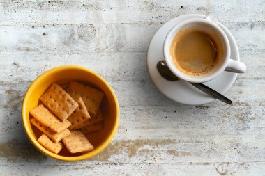 Bir fincan kahve, küçük bir kaşık ve kırsal ahşap masa yüzeyinde bir kraker..