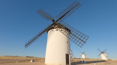 Gün batımında açık mavi gökyüzünün altında eski bir yel değirmeni çiftliğinde daireler çiziyor.