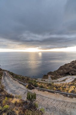 Alacakaranlıkta okyanus üzerinde bulut manzarası ve aşırı eğimli dağ yolu