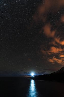 Deniz fenerinin ışığı yıldızlı gökyüzünün altındaki kamerayı gösteriyor.