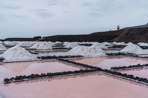 Bright purple salt mine pools with piles of salt near the lighthouse