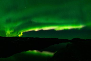 Aurora Borealis mor ve yeşil kirişler göl yansımasını kaplıyor.