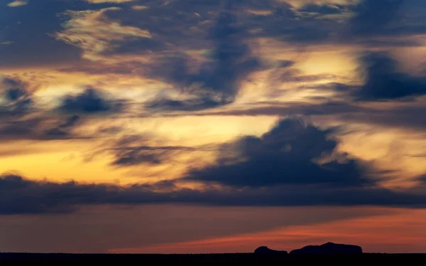 这是一张在黄昏时拍摄的令人震惊的长期曝光照片 它在蓝色和橙色的云彩背景下 捕捉到了地平线上方突出的一座山的宏伟轮廓 — 图库照片