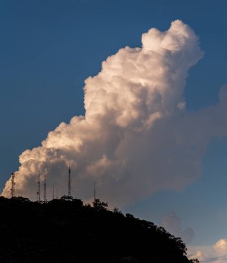 İletişim antenleriyle nefes kesen doğal bir dağ manzarası. Mavi gökyüzünde yükselen dramatik bir bulutun altında dimdik duruyor..
