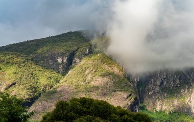 Derin dikey damlaları olan, sabah sisi ile örtülü ve yemyeşil bir ormanla çevrili kayalık bir dağın çarpıcı manzarası. Engebeli arazi ve yüksek tepeler bunu en cesur insanlar için bir macera haline getiriyor.