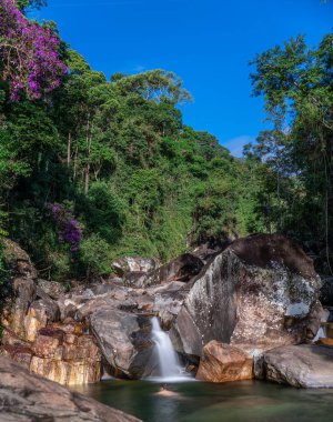 Yükselen bir şelale, bereketli, tropikal yağmur ormanlarındaki büyük taşların üzerinden akar. Bulanık bir insan şelalenin altında yüzerken görülebilir. Evcilleştirilmemiş arazi bir özgürlük hissi veriyor ve...