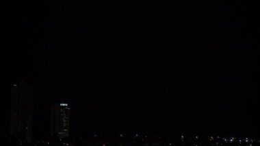 Arka planda yıldırımlar ve gökdelenlerle gece gökyüzünü aydınlatan gök gürültülü bir fırtınanın çarpıcı HLG format videosu, metin örtüleri eklemek için mükemmel.