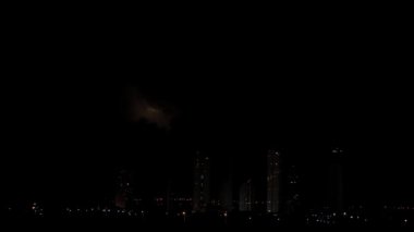 Gece gökyüzündeki karanlık ve heyecan verici fırtınanın yavaş çekim görüntüleri. Şehrin ufuk çizgisi ve gökdelenleri ön planda görülebilir ve metin için yer var. Mimarlık ve aşırı hava durumu.