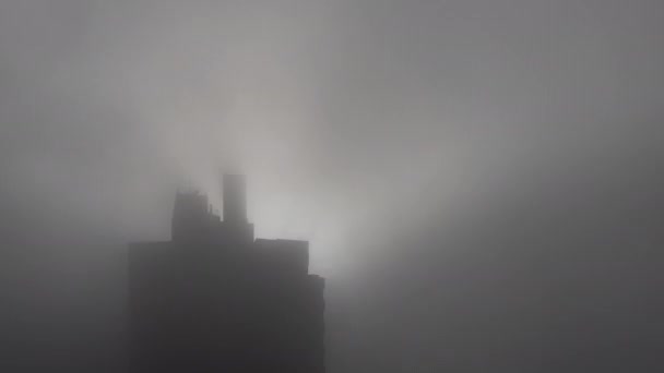 高層ビルのシルエットが濃霧に包まれ 朝日がバックライトに照らされる冬の朝の不気味な気分をキャプチャします 暗く神秘的な感覚を伝えるのに最適です — ストック動画