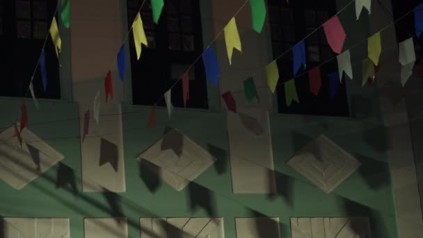 Färgglada Bunting Flaggor Fladdrar Vinden Mot Levande Fasad Natten Med — Stockvideo
