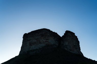 The silhouette of a cross on Father Ignacios Morro in Chapada Diamantina is visible against a clear blue dusk sky, with space for text. clipart