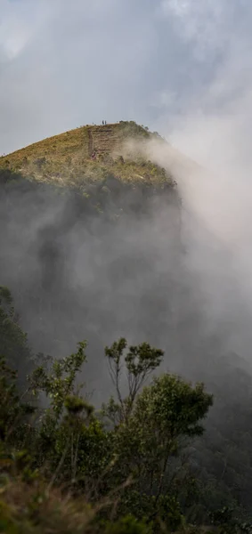 神秘的人物注视着升起的雾气遮掩着山顶上的风景 那是在艰难地爬上最后一道楼梯之后到达的 — 图库照片