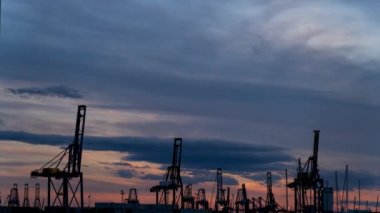 Alacakaranlıkta yoğun bir rıhtımın zamanlaması, vinçlerin gemileri yükleyip indirmesi, metin için yer açması.