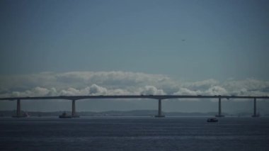Açık gökyüzünün altında, üzerinde metin için yer olan hareketli bir köprünün yanından bir tekne geçiyor..