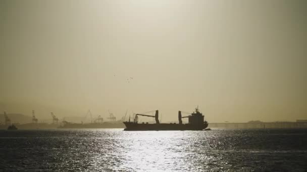 Силуетний Вантажний Корабель Перетинає Воду Відображає Захід Сонця Промисловими Кранами — стокове відео