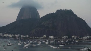 Brezilya Botafogo Körfezi 'ne akşam iniyor. Sisli Sugarloaf Dağı ve yanından geçen bir uçak görünüyor..