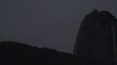 Rio, Brezilya 'daki Sugarloaf Dağı' nın ikonik manzarası. Gün batımında kablolu hatları ve uçakları var..