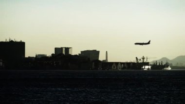Bir uçağın silueti, bir iş bölgesinin günbatımı aydınlık siluetine doğru iniyor..