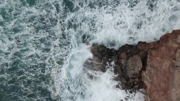 空からの眺めは厳しい海岸の石を絶えず打つ強い波を示します — ストック動画