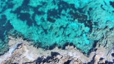 Sahil şeridi boyunca yeşil ve mavi tonlarında kristal berrak bir denizi içeren sakin döngülü bir video..