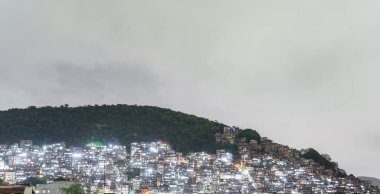 Tepedeki aydınlatılmış kenar mahalleler, kentsel manzaranın katıksız zıtlığını vurguluyor.