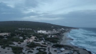 Hava görüntüleri, dolunay altında Formenteras sahili boyunca uzanan koyların ve mimarinin alacakaranlık manzarasını gösteriyor..