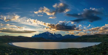 Torres del Paine 'deki sakin dağ gölünün üzerindeki büyüleyici günbatımı ve bulutlu manzara