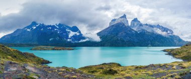 Karlı dağları ve turkuaz gölü olan sakin bir manzara. Cuernos del Paine