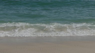 Yumuşak deniz dalgaları berrak gökyüzünün altında el değmemiş kumlu bir plaja vuruyor..