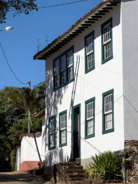 Yeşil çerçeveli camları olan büyüleyici beyaz bir ev, dingin mavi gökyüzüne karşı serin bir gün ışığında güneşleniyor..