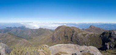 Yuvarlanan dağ sıralarının resimli bir sahnesi. Altında bulutlar ve yukarıda mavi bir gökyüzü var..