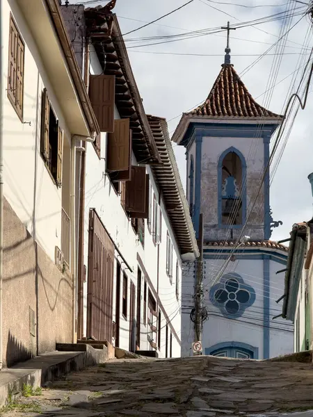 stock image A vintage cobbled street ascends towards an old church with a blue facade in Brazil.