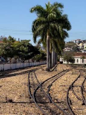 Eski demiryolu rayları açık mavi gökyüzünün altında yemyeşil bir palmiye ağacının yanında birleşir..