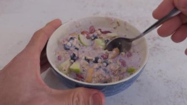 Elma ve böğürtlenli yulaf ezmesi kepçesiyle kaşığı kameraya doğru hareket ettiren eller..