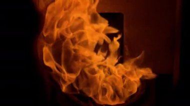 Slow-motion video of a vibrant orange flame from a pellet stove in darkness, offering warmth and room for text.