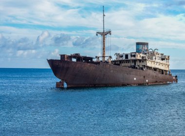 Mavi okyanusta paslanan bir gemi enkazı, aydınlık ve bulutlu bir günde terk edilmeyi ve gizemi simgeler..