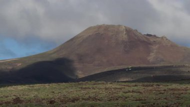 Lanzarote 'deki volkanik kraterin nefes kesici bir görüntüsü, yemyeşil ve bulutlar oluşturan volkanik bir koni..
