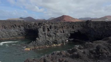 Yavaş çekimde Los Hervideros 'taki Lanzarotes volkanik sahilini yakalıyor. Çarpışan dalgaları ve ikonik bölgeyi keşfeden turistleri vurguluyor..