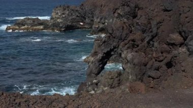 Yavaş çekim videosu engebeli oluşumları ve okyanus dalgalarının kıyıya çarptığı karanlık volkanik kaya kıyılarını gösteriyor..