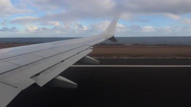 Okyanusa yakın pisti olan adadaki sahil havalimanından kalkış sırasında yolcu penceresinden uçak kanadının görüntüsü.
