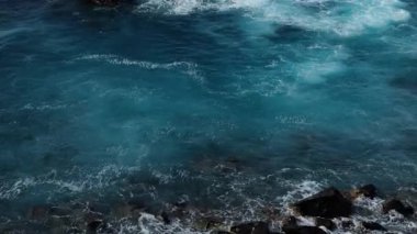 Volkanik bir kıyı şeridine vuran yeşil okyanus dalgalarının yavaş çekim videosu metin örtüsü için büyüleyici bir sahne oluşturuyor..