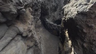 Ağır çekimde, volkanik kayaların üzerinde okyanus çukuruna bakan bir balkona doğru yürürken, aşağıda hafif su hareketleri görülüyor..