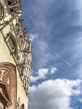Gotik bir katedral cephe kulesi mavi gökyüzünde bulutlarla, tarihi ihtişamı ve karmaşık mimariyi gözler önüne seriyor..