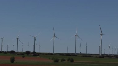 Bir panoramik video mavi gökyüzünün altındaki kırsal çayırlarda dönen rüzgar türbinlerinin sürdürülebilir enerji üretimini gösteriyor..