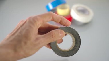 Bir el, kirli gri koli bandının yapışkan gücünü arka planda bulanık renkli bantlarla yakından test eder..