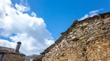 Dinamik zaman çizelgesi, hızlı hareket eden bulutların altında tarihi kırsal mimariyi ve doğayı vurgulayan eski bir kiremitli çatı ve taş cephe olduğunu gösteriyor..