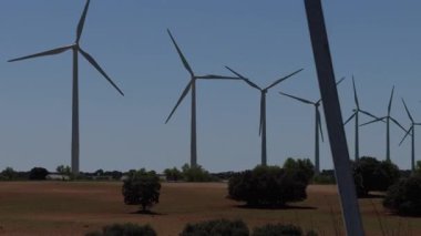 Rüzgâr türbinleri açık mavi gökyüzünün altında durarak temiz enerji ve çevresel sürdürülebilirliğin önemini sembolize eder..
